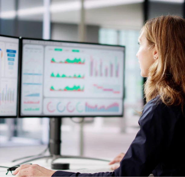 Analyst reviewing charts on dual monitors representing advanced economic analytics, forecasting models and data-driven insights.